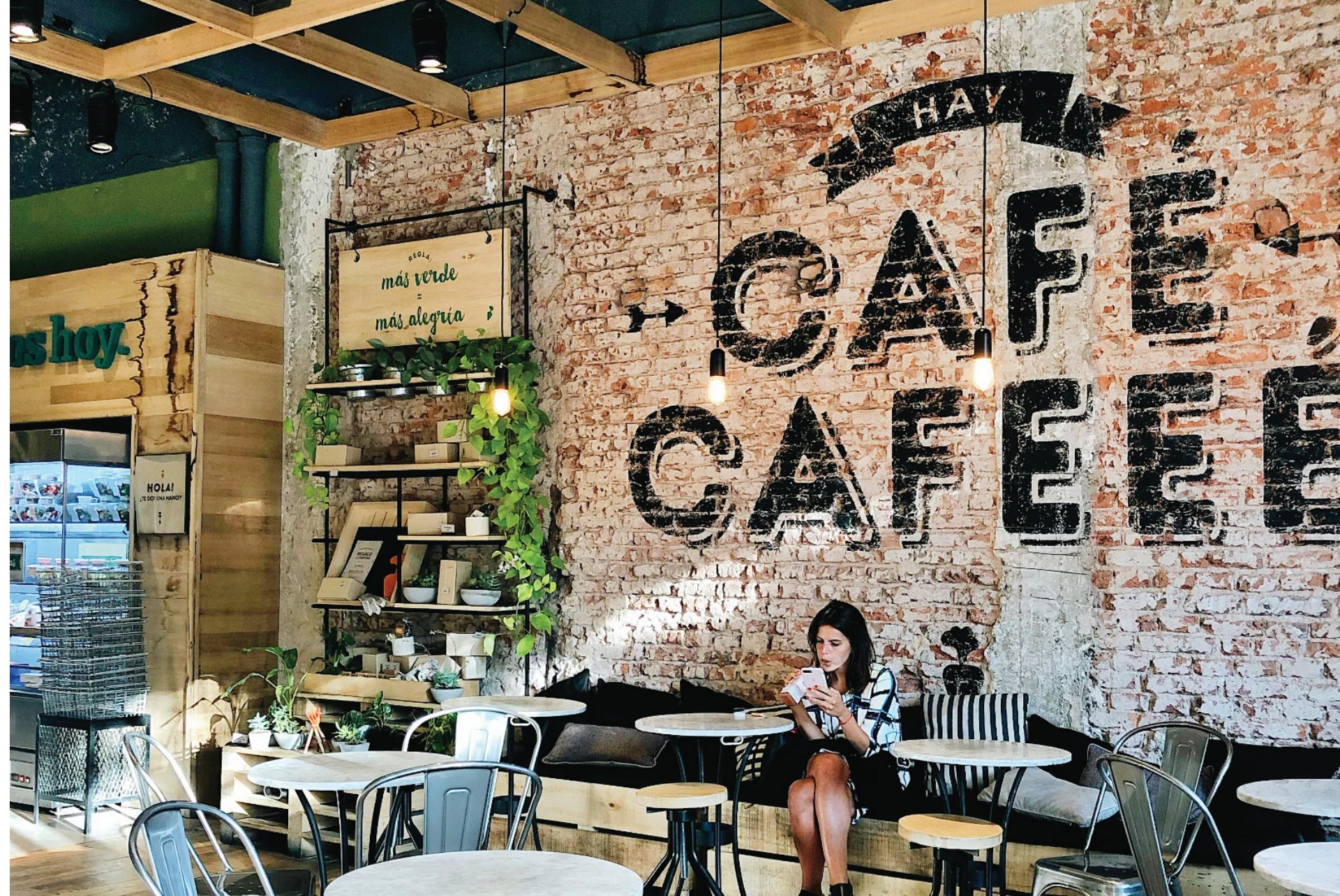 Green Eat exposed brick wall with hand-painted CAFE CAFEEE typography, woman seated